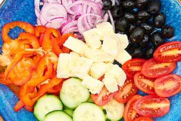 Greek salad with Cherry tomatoes, cucumber, peppers, olives, Greek feta cheese, red onions in the blue plate with white background