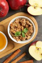 Delicious apple crisp in bowl, fresh fruits, cinnamon sticks, honey and mint on grey table, flat lay