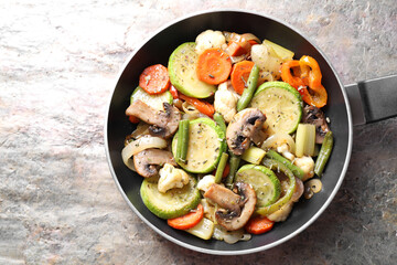 Different vegetables and mushrooms in frying pan on grey textured table, top view
