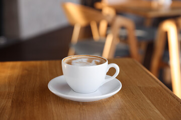 Cup of aromatic coffee on wooden table in cafe, closeup
