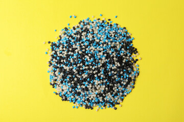 Pile of colorful plastic granules on yellow background, top view