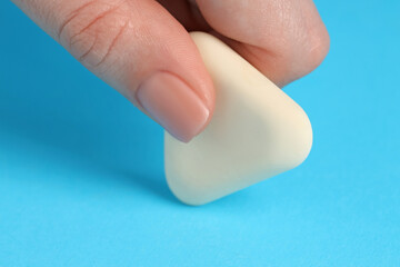 Woman using eraser on light blue background, closeup