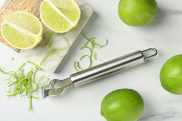 Lime zest, fresh fruits and zester tool on white marble table, flat lay