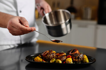 Professional chef adding sauce to delicious dish at table indoors, closeup