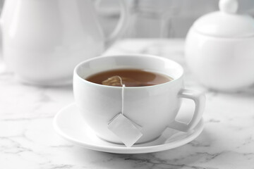 Tea bag in cup with hot drink on light marble table, closeup