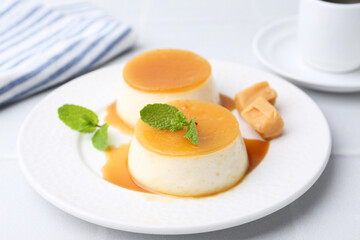 Tasty puddings with caramel sauce served on white tiled table, closeup