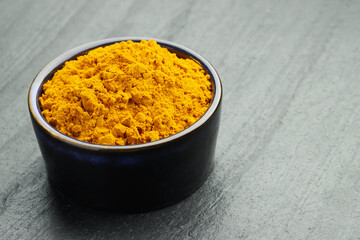 Turmeric powder in bowl on grey table, closeup. Space for text