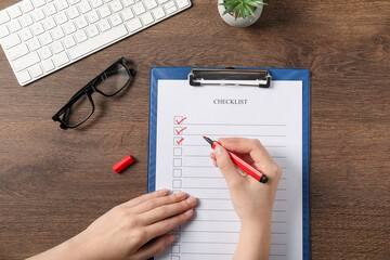 Woman filling Checklist at wooden table, top view