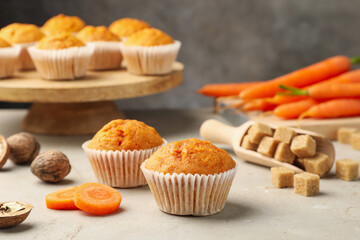Tasty carrot muffins, fresh vegetables, sugar and walnuts on light grey table, closeup