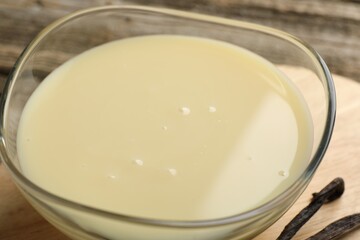 Tasty condensed milk and vanilla pods on table, closeup