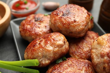 Delicious patties with green onions on black table, closeup