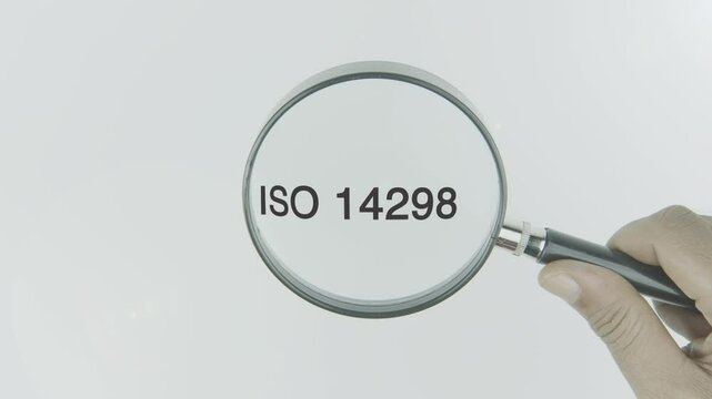 ISO 14298 text or word highlighted by a magnifying glass in a hand on a white background, symbolizing security in the printing process, with a focus on anti-counterfeiting and quality control