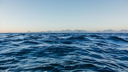 The open ocean under a clear blue sky, with distant mountains on the horizon and soft waves rolling by