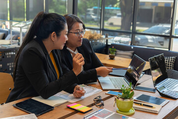 Two happy busy female employees working together using computer planning project.