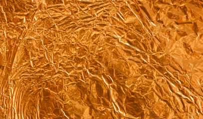 Crumpled gold foil as background with light and shadow texture details. Shiny gold foil wallpaper.