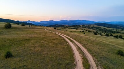 Fototapeta premium A winding dirt road snakes through a vast, open landscape towards distant mountains, evoking a sense of adventure and tranquility.
