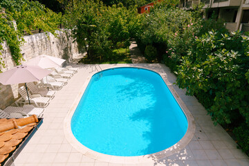 White sun loungers stand under umbrellas by the pool among flowering trees in the courtyard