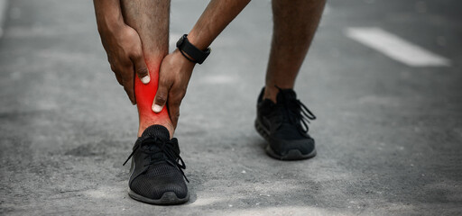 Unrecognizable young jogger feeling pain in his ankle during his morning run at park, close up....