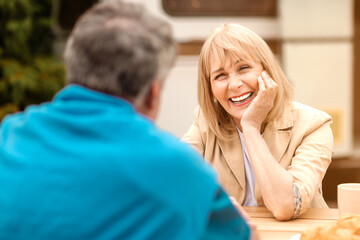 Fototapeta premium Happy mature woman talking to her husband during tasty breakfast with coffee and croissants at campground