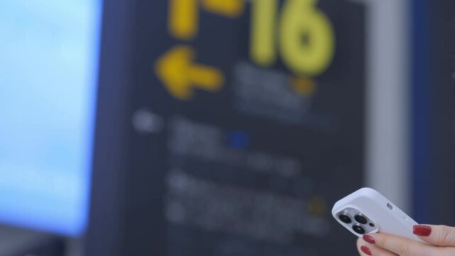 Woman is holding a white iPhone in front of a sign that says 16. The sign is on a wall and has arrows pointing to the right