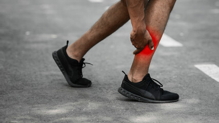 Millennial runner holding his injured ankle on road outdoors, closeup of legs. Blank space. Panorama