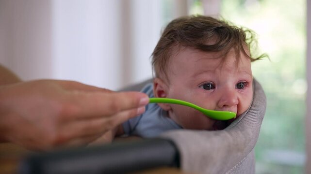 Baby reacting with teary eyes while being fed, resisting spoonful of food, showing discomfort, strong emotional response, early childhood feeding challenge