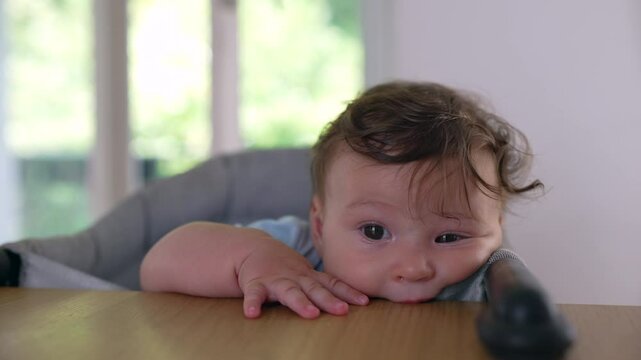 Baby chewing on table edge while sitting in high chair, teething exploration, curious infant biting furniture, playful discovery, natural light indoor home setting