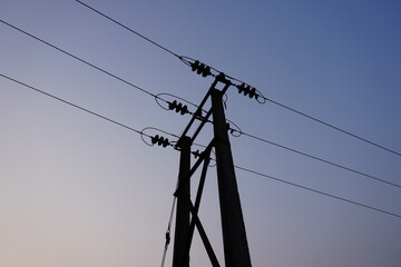 The top of a power transmission pole with multiple lines against the clear sky background 