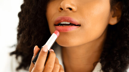 Daily Makeup. Unrecognizable black woman in bathrobe applying pink lipstick, taking care of her lips at home, cropped image, closeup