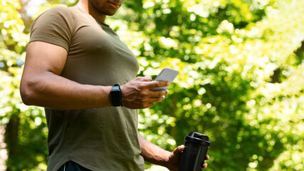Sporty guy taking break from his training and surfing net on smartphone at park, copy space