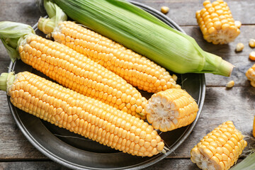 Plate with fresh corn cobs on grey wooden table, closeup