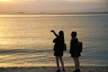 夕焼けと海岸線で記念撮影する女学生