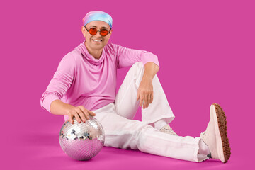 Cool mature man with disco ball sitting on purple background
