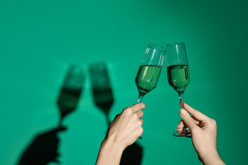 Female hands with glasses of champagne on green background
