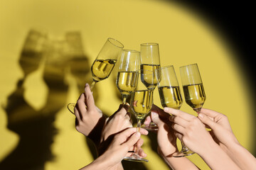 Female hands with glasses of champagne on yellow background