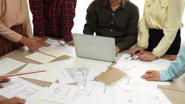 Architect and safety engineer discussion about building blueprint displaying on laptop on table with architectural document and wooden block scatter around at modern office. Closeup. Delineation.