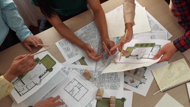 Smart architect and safety engineer discussion about building blueprint on table with architectural document, measurement tools and wooden block scatter around at modern office. Closeup. Delineation.
