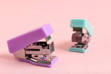 Different small staplers on pink background