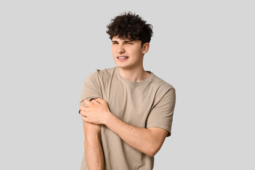 Young man with allergy scratching himself on grey background