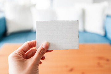 hand holding small cardboard label with blank copy space in front of stylish sofa and coffee table