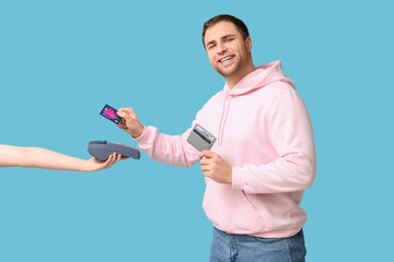 Young man paying with credit card via payment terminal on blue background