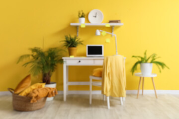 Fototapeta premium Stylish room with workplace, modern laptop, chair and clock on yellow wall, blurred view