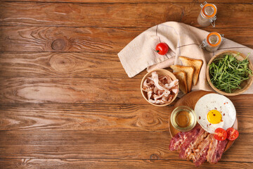 Plate with fried egg, toasts and raw bacon on wooden background. Top view