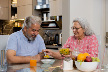 Happy retired senior indian couple eating healthy breakfast together, Elderly husband wife enjoy...