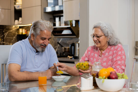 Happy retired senior indian couple eating healthy breakfast together, Elderly husband wife enjoy food at table, Love and bonding. Retirement life.