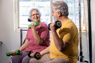 Active indian senior couple doing exercises in gym, Vital elderly people weight lifting training with dumbbells at health club to stay fit.