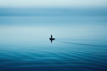 Fototapeta premium A Solitary Bird Perched On A Tiny Rock In The Vast, Tranquil Ocean Under A Serene, Pale Sky