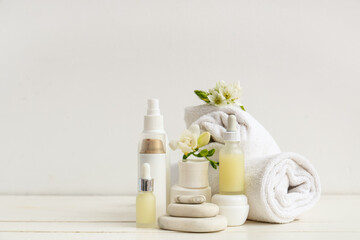 Composition with cosmetic products, spa stones, clean towels and flowers on light wooden table