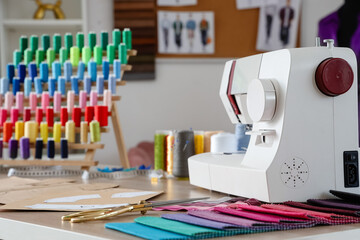 Sewing machine with patterns and fabric samples on tailor's table in atelier, closeup