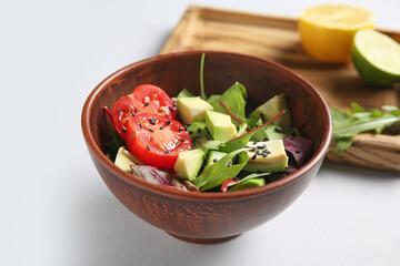 Bowl of tasty avocado salad with cherry tomato and sesame seeds on grey background